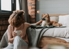 Woman-sitting-at-the-edge-of-the-bed-and-petting-a-dog-laying-on-the-bed